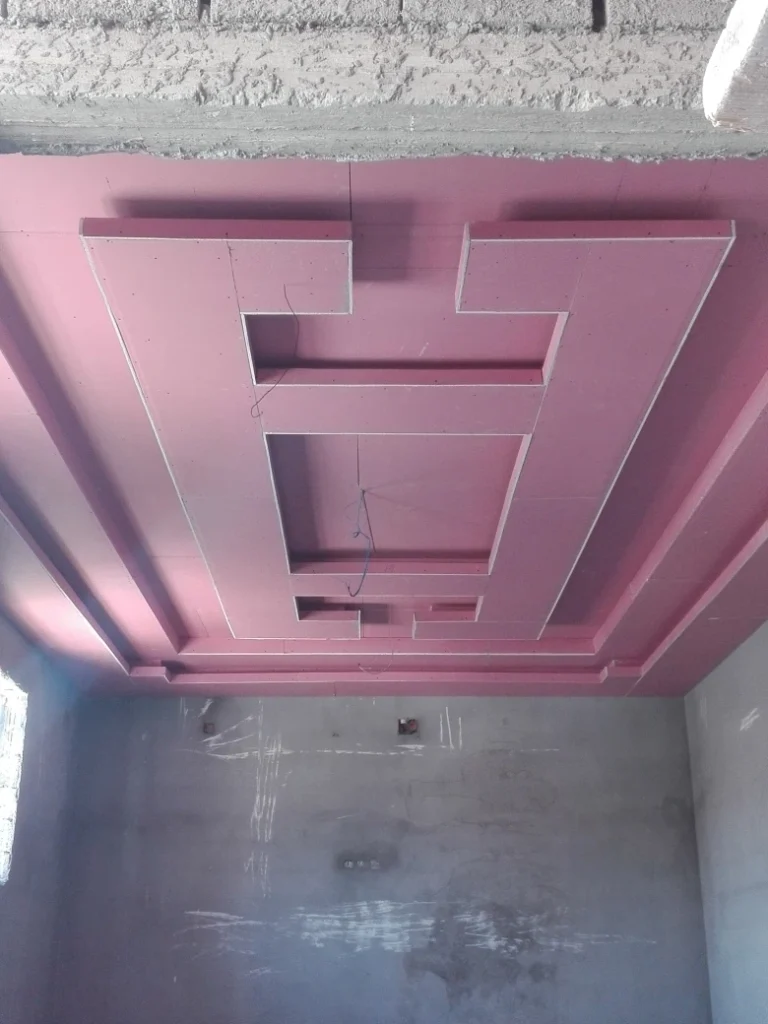 سقف جبس بورد قيد التنفيذ باللون الوردي، بتصميم متدرّج يحتوي على مستويات بارزة وفتحات مخصّصة للإضاءة المخفية